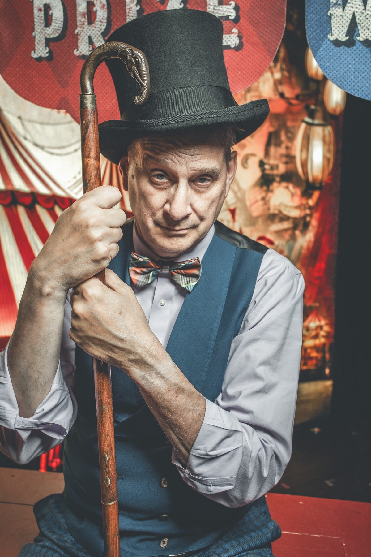 David Williamson as a circus ringmaster, leaning on a cane with a playful expression
