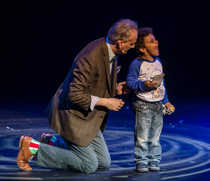 David Williamson kneels beside a delighted young volunteer during a stage performance