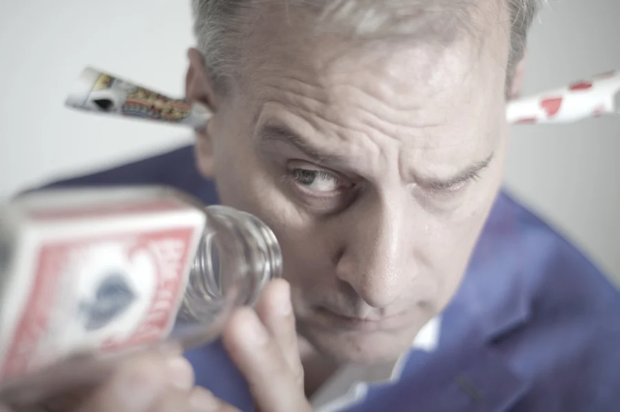 David Williamson holding a bottle and fanned playing cards near his face